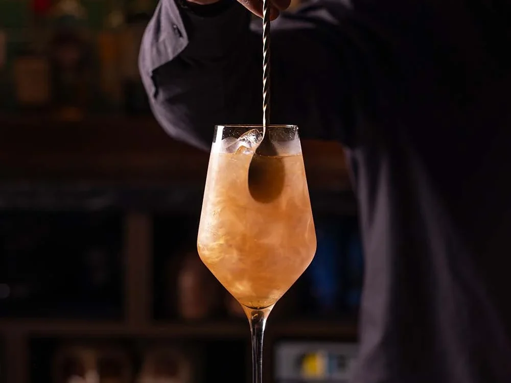 A bartender stirring a cocktail in a tall glass at Siamais