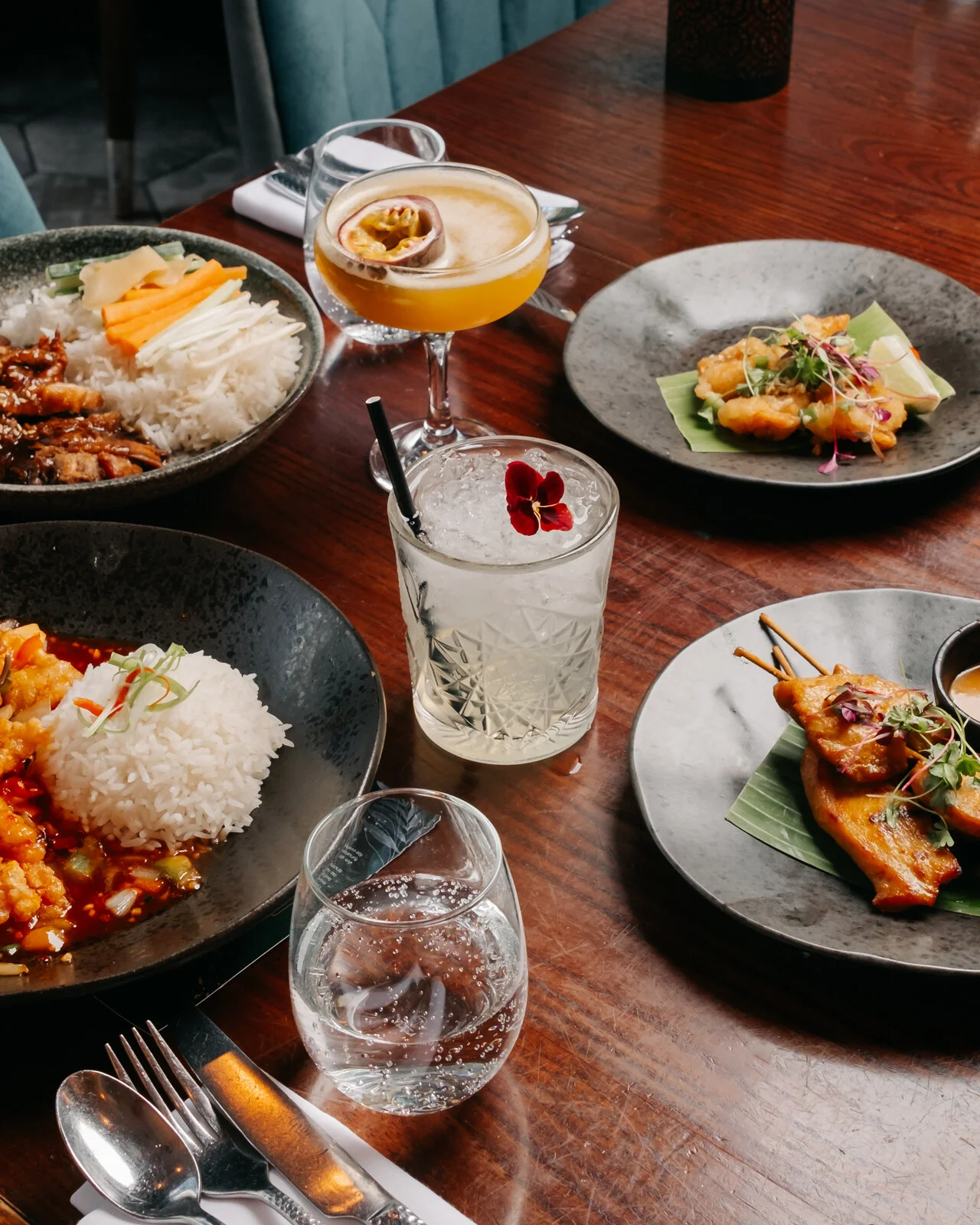 Thai sharing dishes, satay and cocktails laid out on a table at Siamais